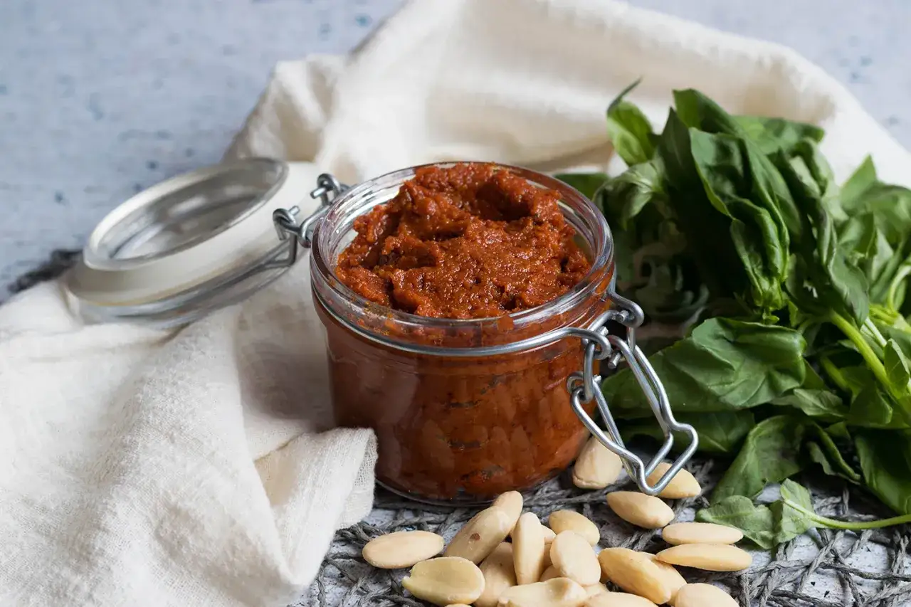 Tarro de pesto rosso casero con albahaca fresca y almendras.