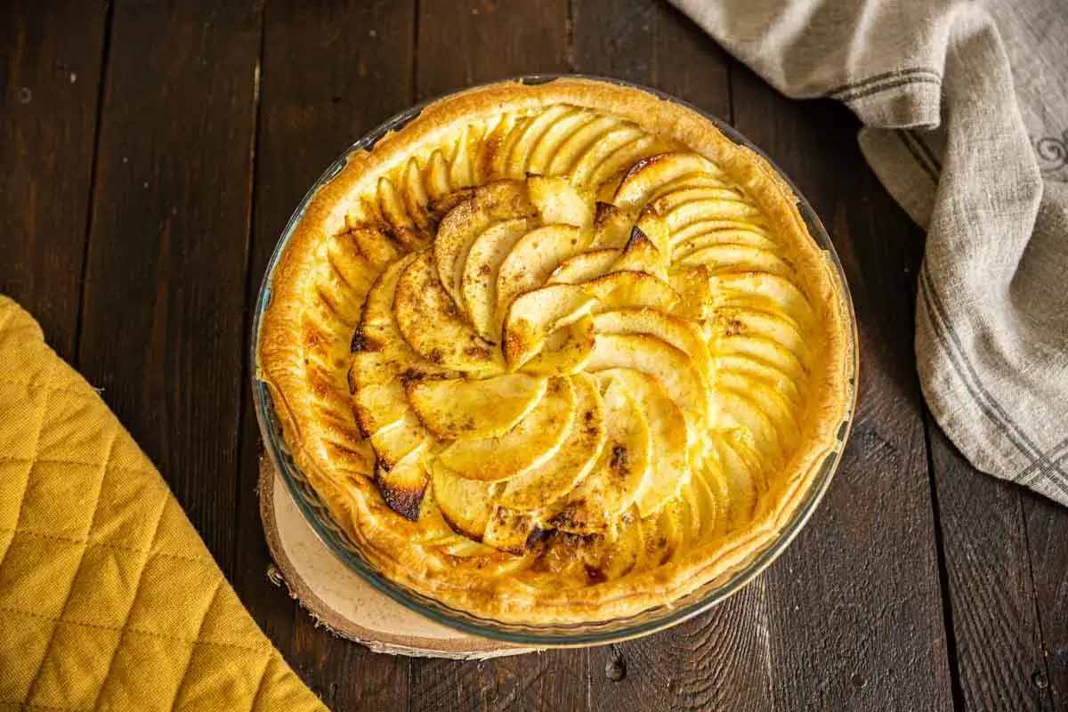 Une tarte aux pommes simple, dorée et appétissante, avec des pommes finement tranchées disposées en spirale sur une pâte croustillante.