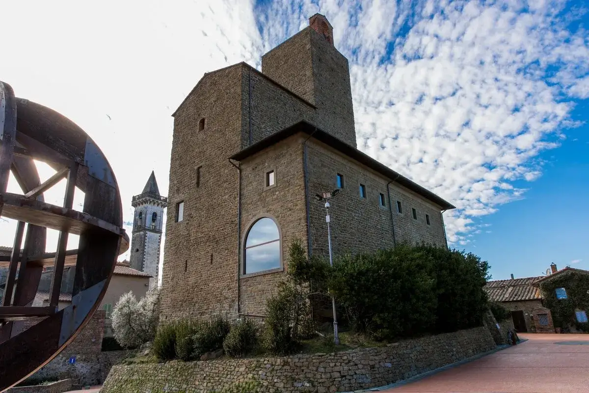 Antica torre nel vinci centro storico, con una ruota di mulino in primo piano e un campanile sullo sfondo.