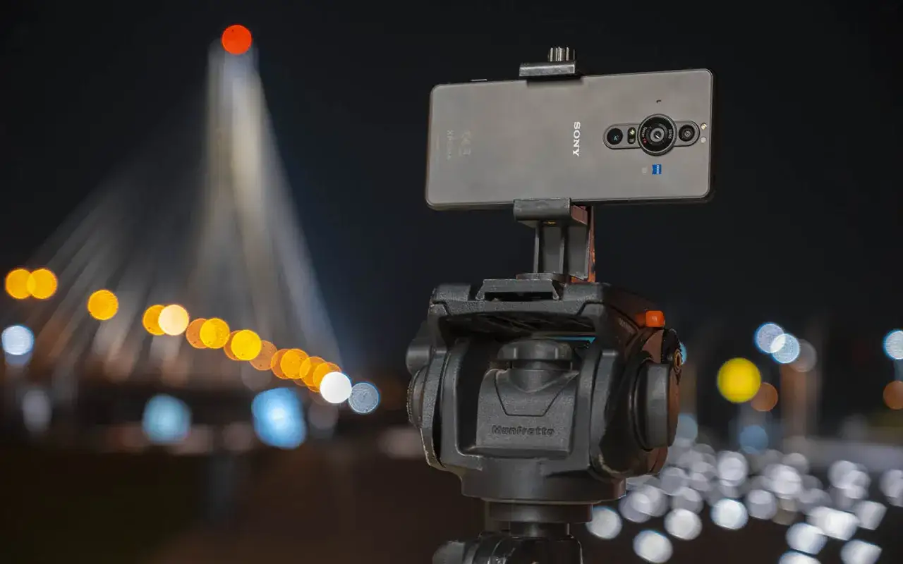 Sony Xperia Pro i na statywie Manfrotto, nocą, z rozmytymi światłami miasta w tle.