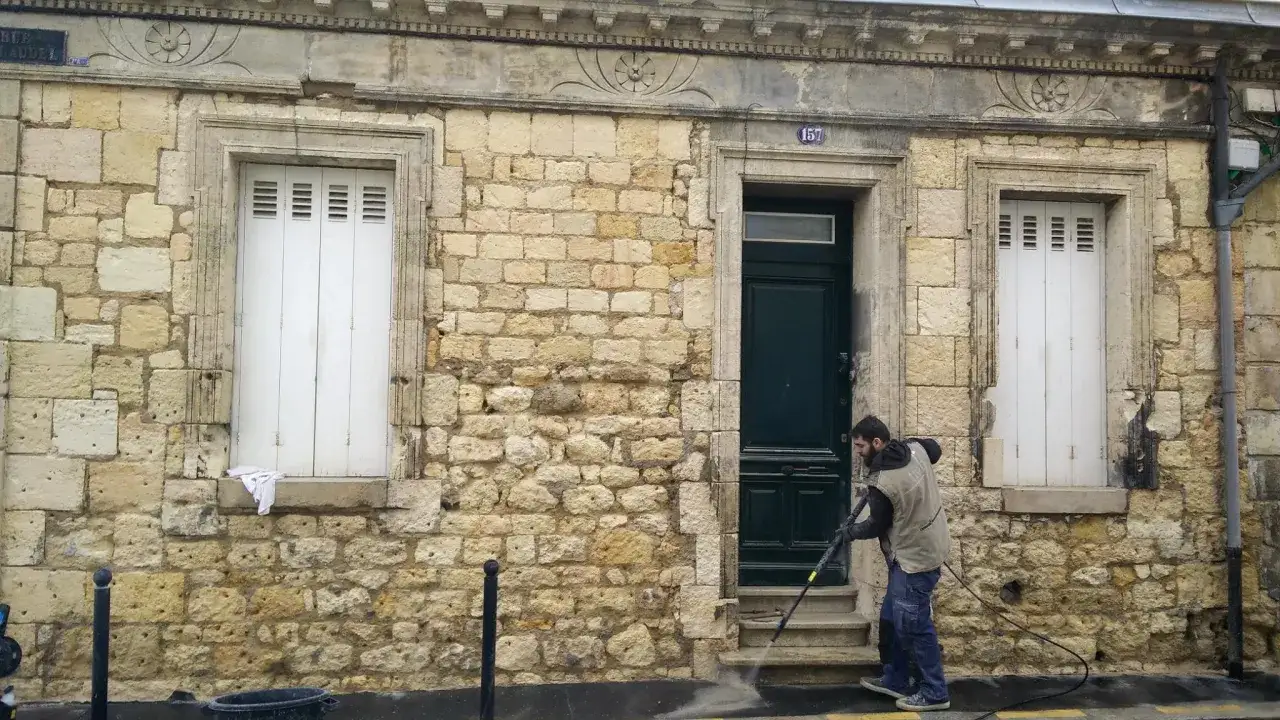 Un homme nettoie la fa&ccedil;ade d'une maison bordeaux typique avec un nettoyeur haute pression.