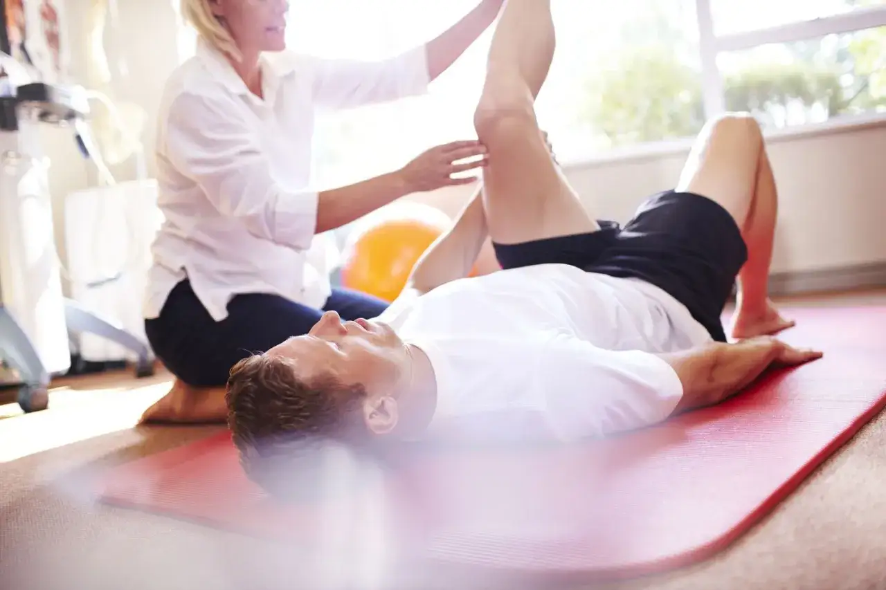 Fizjoterapeuta pomaga pacjentowi w rehabilitacji nóg ćwiczenia na macie.