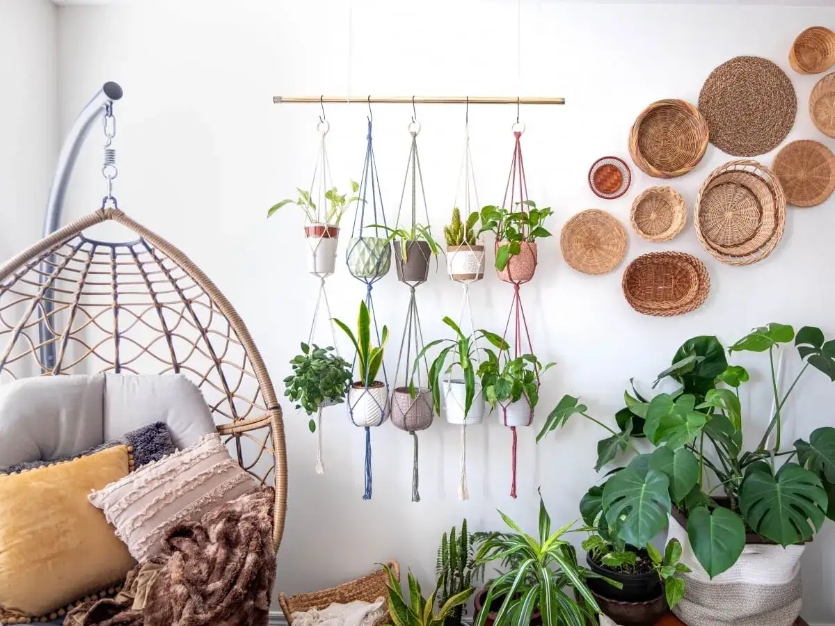 Przytulny balkon w stylu boho: wiszący fotel z poduszkami, makramy z roślinami i plecione kosze na ścianie tworzą relaksującą atmosferę.
