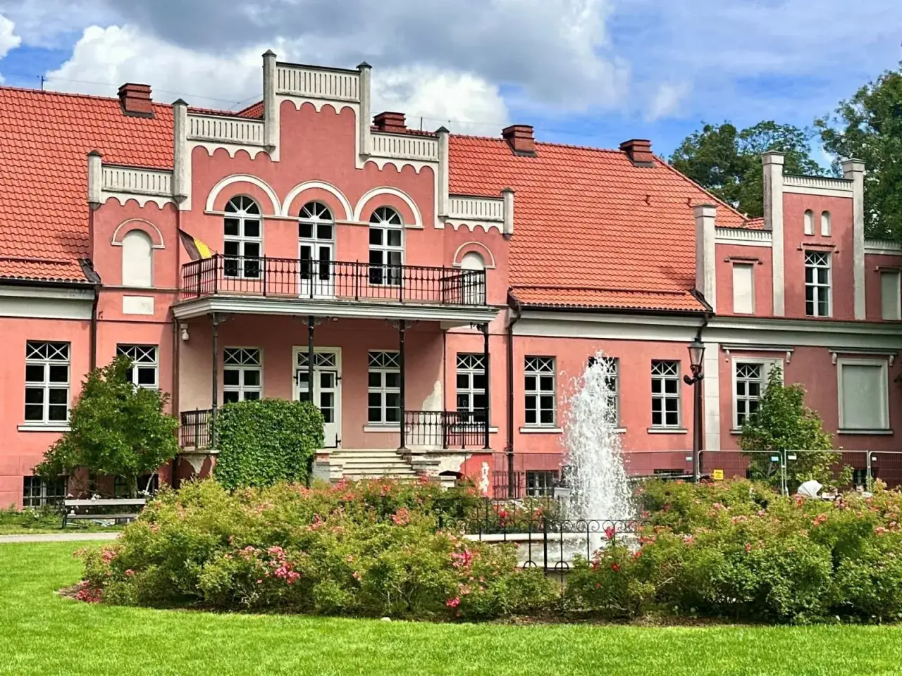 Pałac Przebendowskich w Wejherowie, r&oacute;żowy, z fontanną i kwitnącymi krzewami r&oacute;ż.