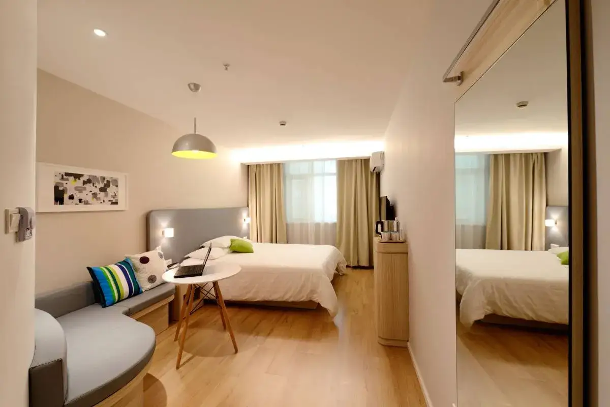 Habitaci&oacute;n estrecha y alargada con cama, sof&aacute; curvo, mesa con port&aacute;til y espejo de cuerpo entero.