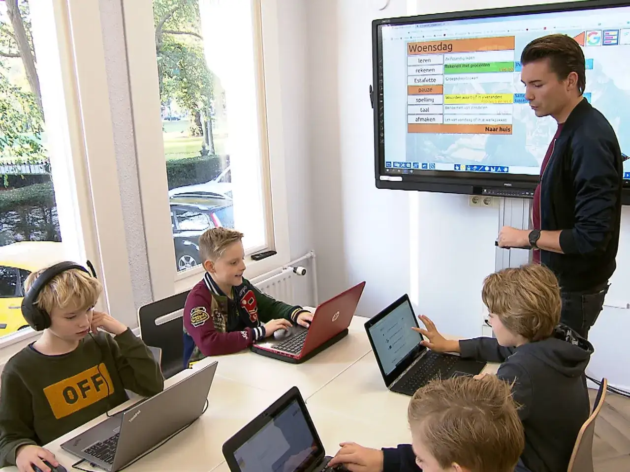 Kinderen leren op laptops, een leraar geeft uitleg bij een digibord. De focus ligt op educatie, wat de investering in particulier onderwijs kosten rechtvaardigt.