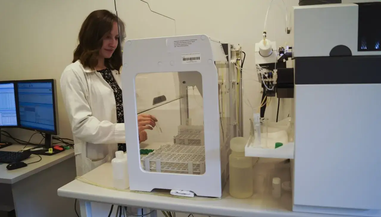 Naukowczyni w białej kurtce laboratoryjnej prowadzi badanie miodu, obsługując nowoczesny sprzęt analityczny.
