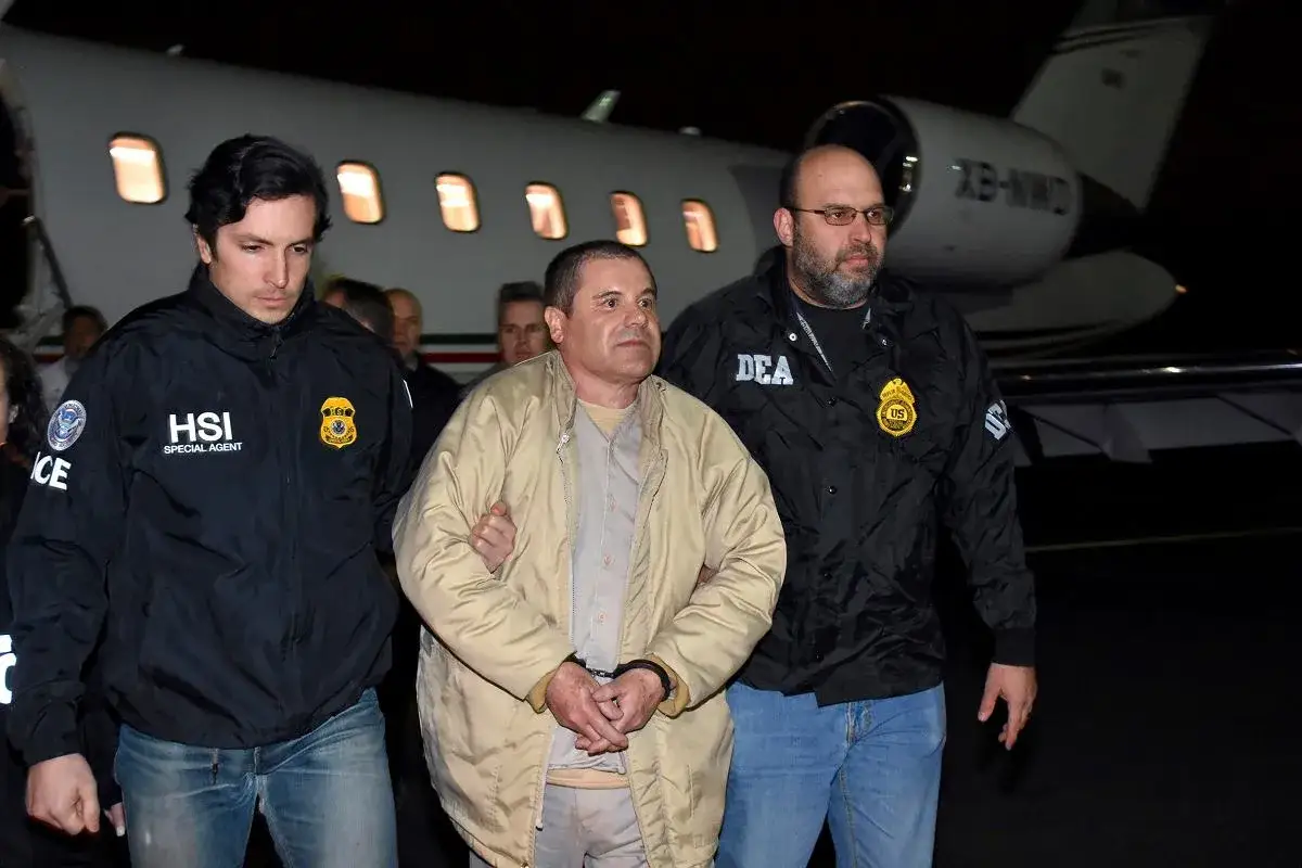 El Chapo, skuty kajdankami, prowadzony przez agentów HSI i DEA do samolotu.