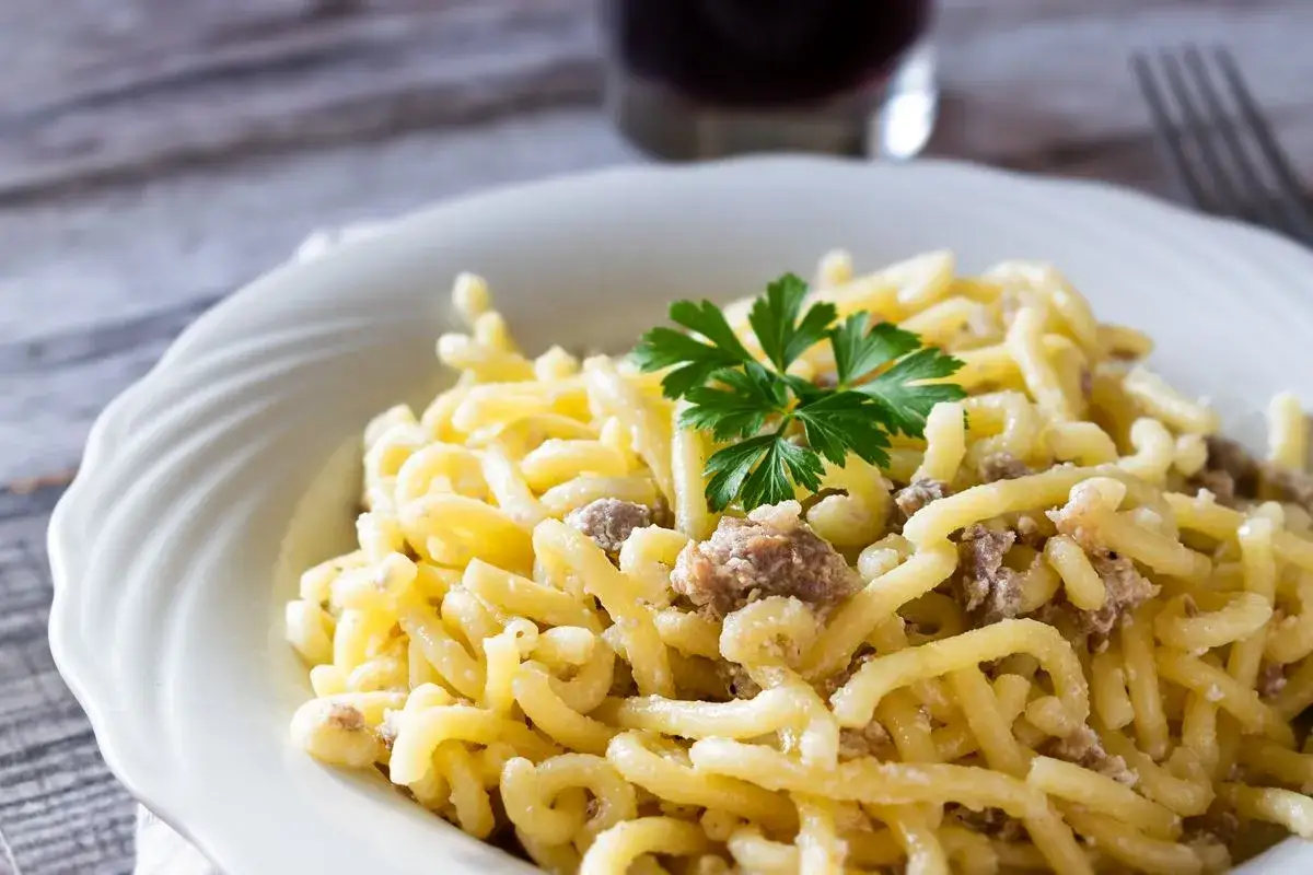 Un piatto di pasta con salsiccia, condita con un rametto di prezzemolo fresco, su un tavolo di legno.