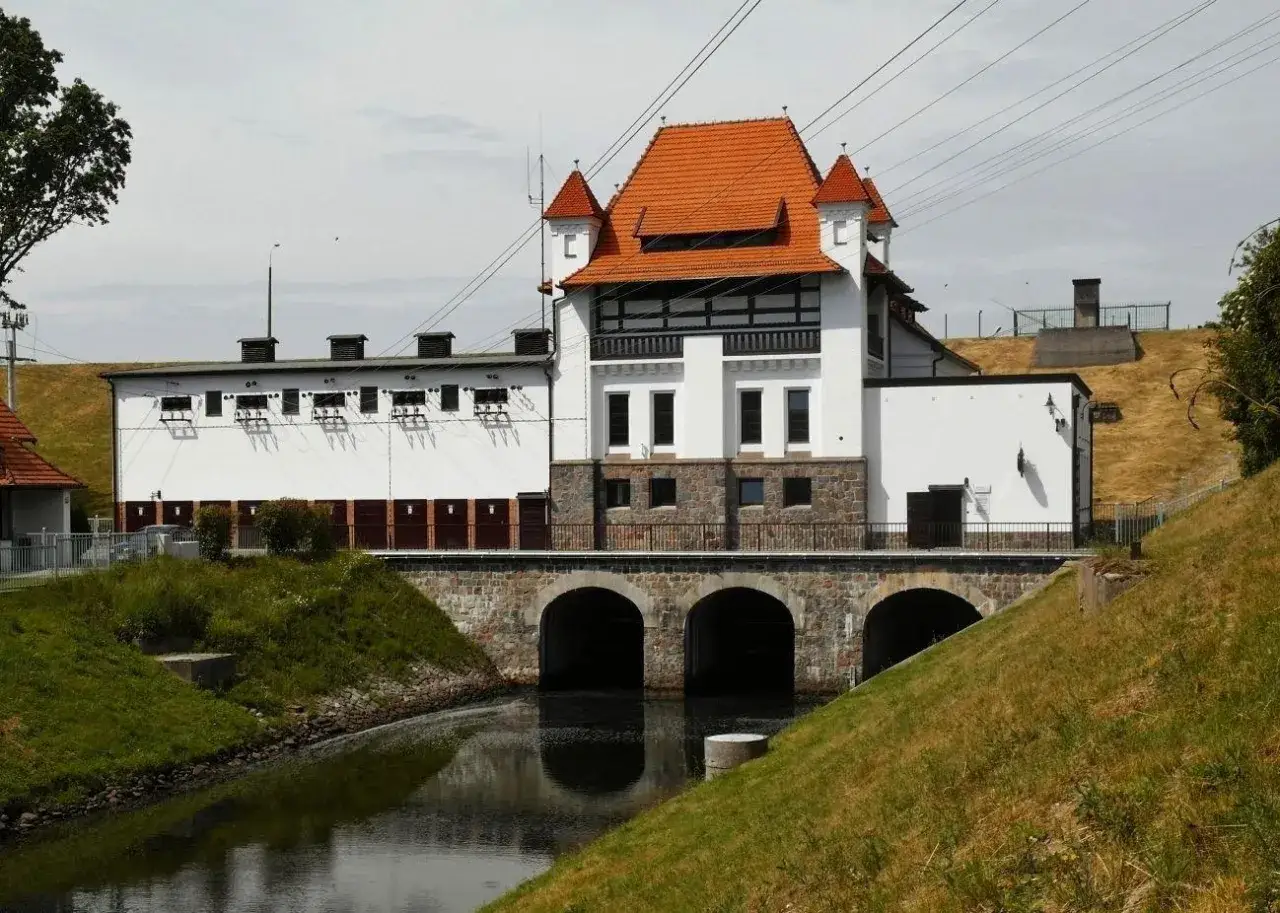 Straszynska elektrownia wodna z charakterystycznym czerwonym dachem i kamiennym mostem nad kanałem.