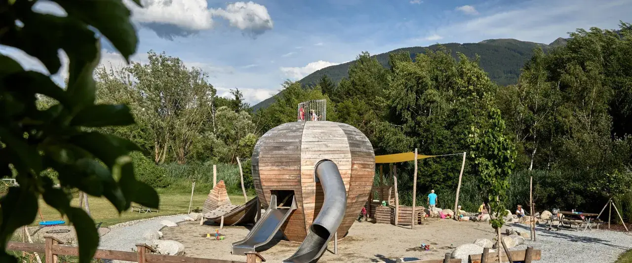 Un fantastico parco avventura in Alto Adige con una struttura a forma di sfera in legno, scivoli e aree gioco per bambini.