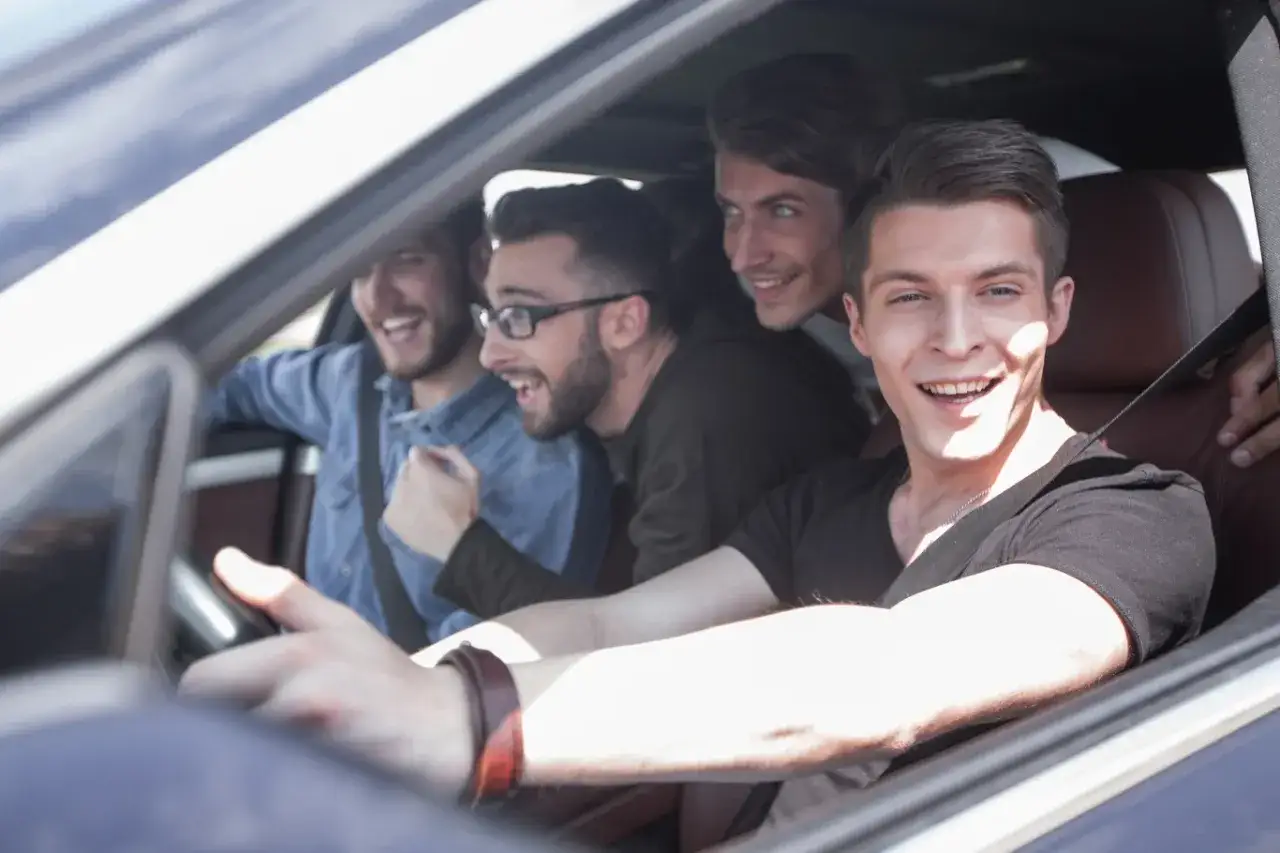 Czterech uśmiechniętych młodych mężczyzn w samochodzie. Kierowca, który niedawno zdobył prawo jazdy 17 lat, cieszy się jazdą z przyjaciółmi.