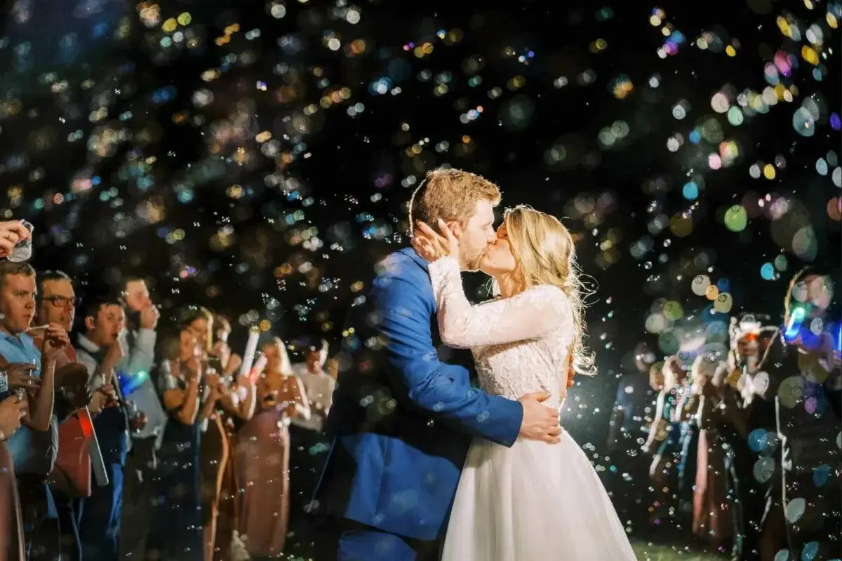 Brautpaar k&uuml;sst sich im Seifenblasenregen. G&auml;ste mit Lichtern im Hintergrund. Ein magischer Moment beim **Auszug Hochzeit**.