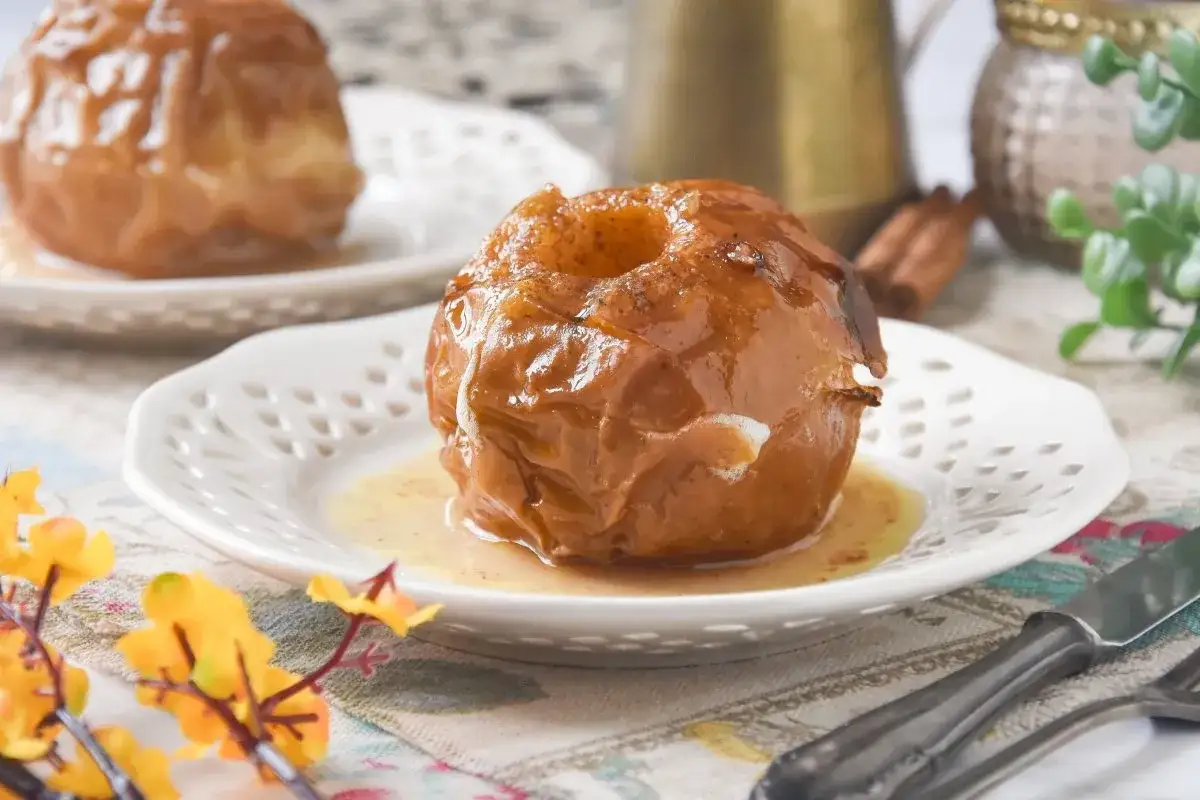 Manzanas al horno glaseadas, servidas en un plato blanco con un sirope dulce y canela.