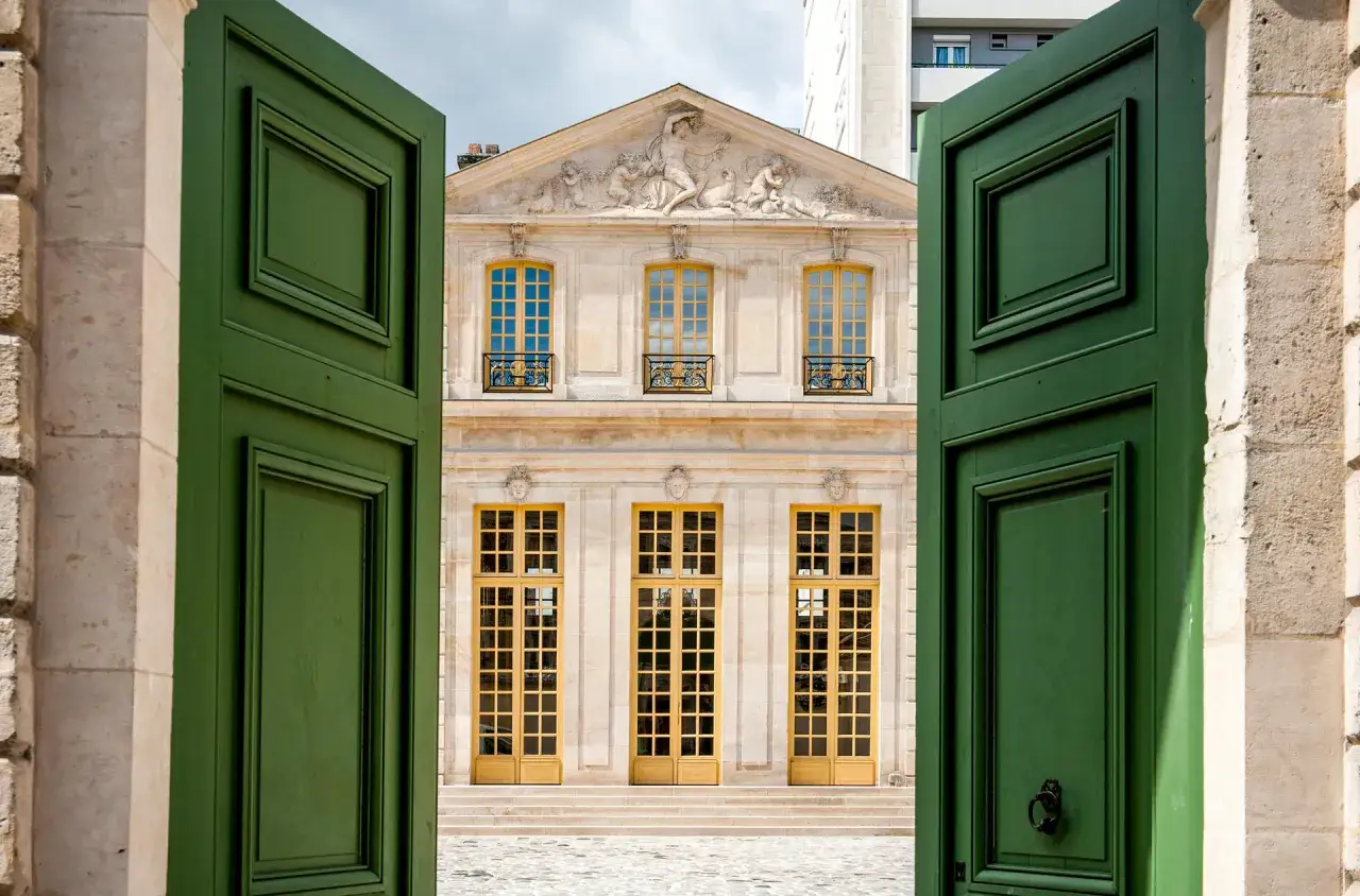 Vue sur le pavillon Vend&ocirc;me &agrave; Paris, &agrave; travers de grandes portes vertes ouvertes. L'architecture classique et les fen&ecirc;tres dor&eacute;es invitent &agrave; la d&eacute;couverte.