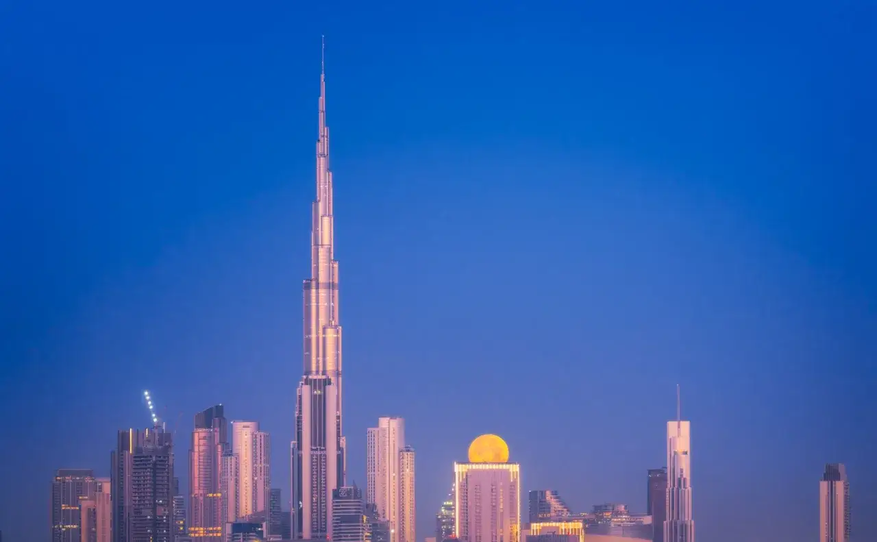 Dubaj najwyższy budynek, Burj Khalifa, lśni w blasku księżyca. Miasto rozświetlone, nocne niebo granatowe.