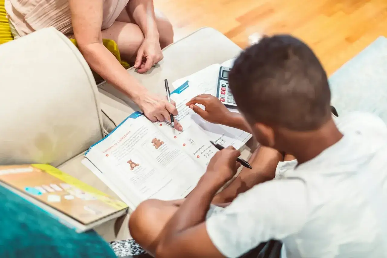 Chłopiec z dysleksją matematyczną z pomocą nauczycielki rozwiązuje zadania z podręcznika.
