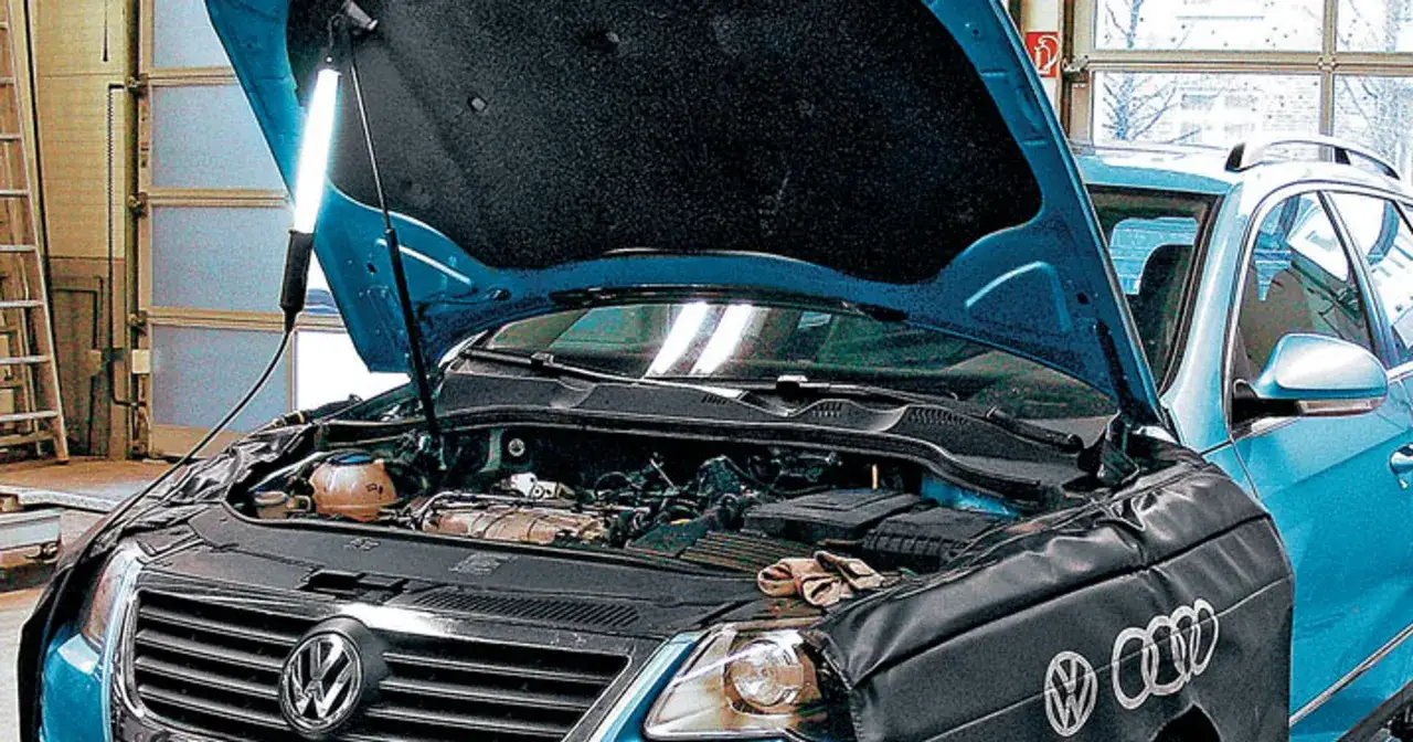 Pod maską niebieskiego auta z silnikiem 2.0 TDI mechanik oświetla silnik lampą.