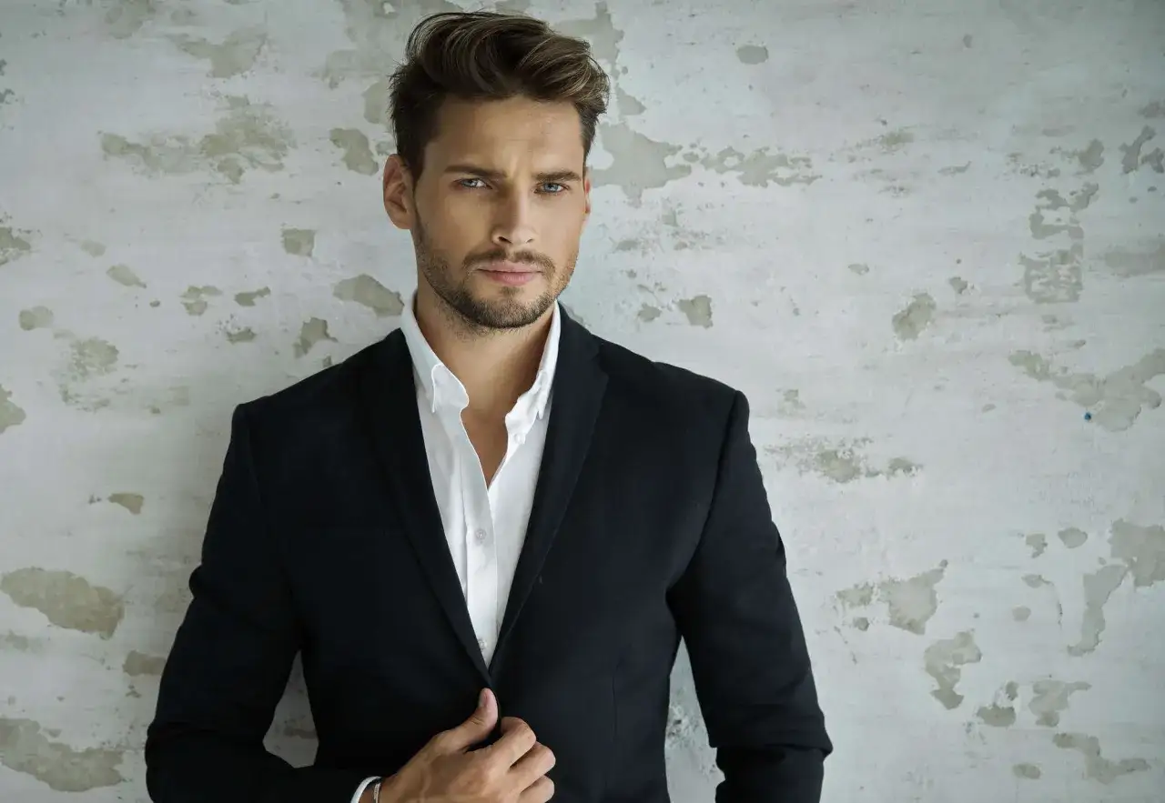 Uomo con un elegante ciuffo a tendina, indossa una giacca nera e camicia bianca. Sguardo intenso.