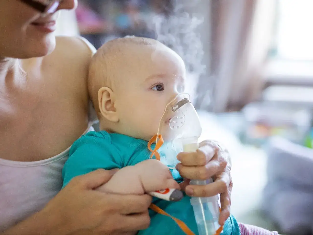 Mama pomaga dziecku w inhalacji solą fizjologiczną. Para z nebulizatora otula malucha.