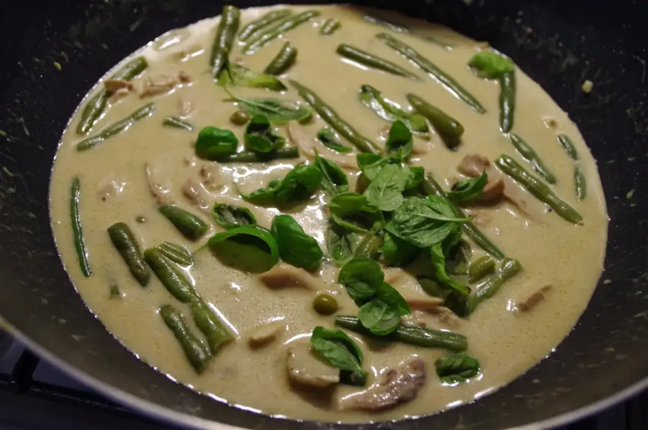 Zielona pasta curry z kurczakiem, fasolką szparagową i świeżą bazylią gotująca się na patelni.