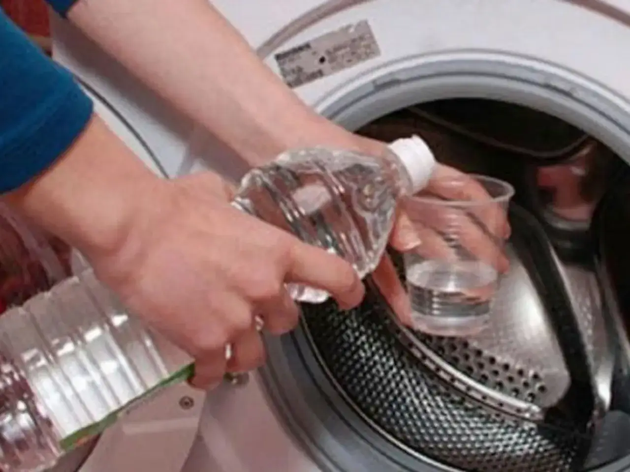 Manos vierten líquido de una botella a un vaso dentro de una lavadora. ¡Cuidado! el bicarbonato estropea la ropa de color.