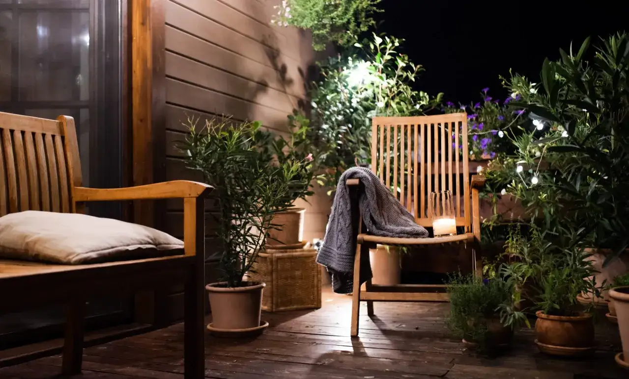 Ambiance chaleureuse sur une petite terrasse : chaises en bois, coussin, plaid, bougie et plantes vertes. Une belle deco petite terrasse pour des soirées paisibles.