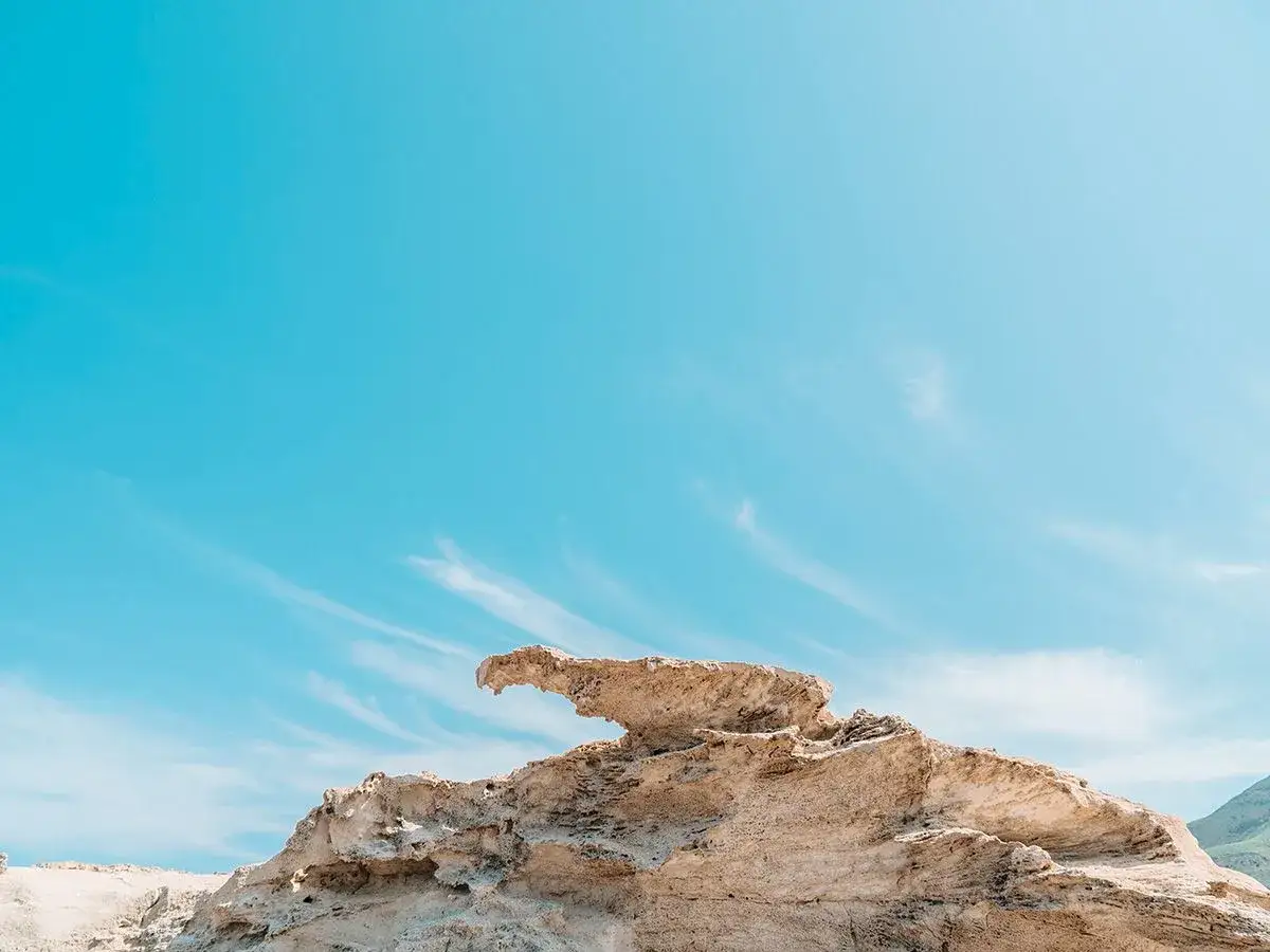Formaciones rocosas erosionadas en una playa de arcos bajo un cielo azul vibrante con nubes tenues.