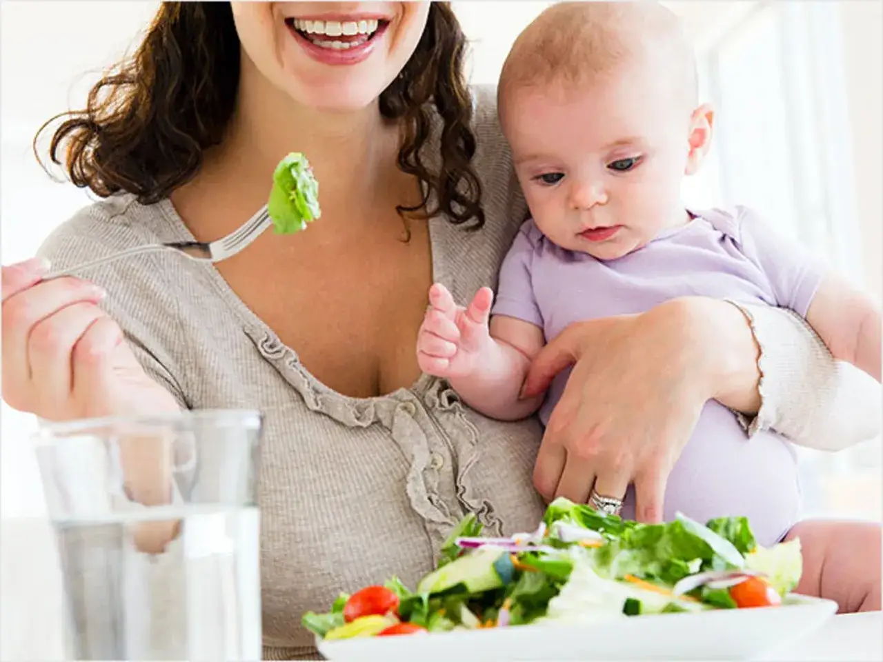 Glad mamma &auml;ter en fr&auml;sch sallad, en del av mat vid amning, medan hon h&aring;ller sitt barn.