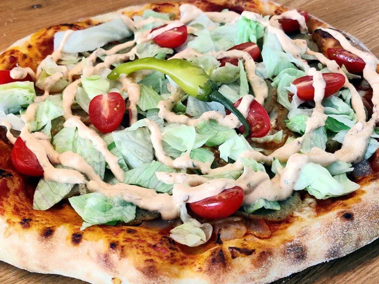 En pizza i Sverige med krispig sallad, körsbärstomater, en grön chili och en krämig dressing.