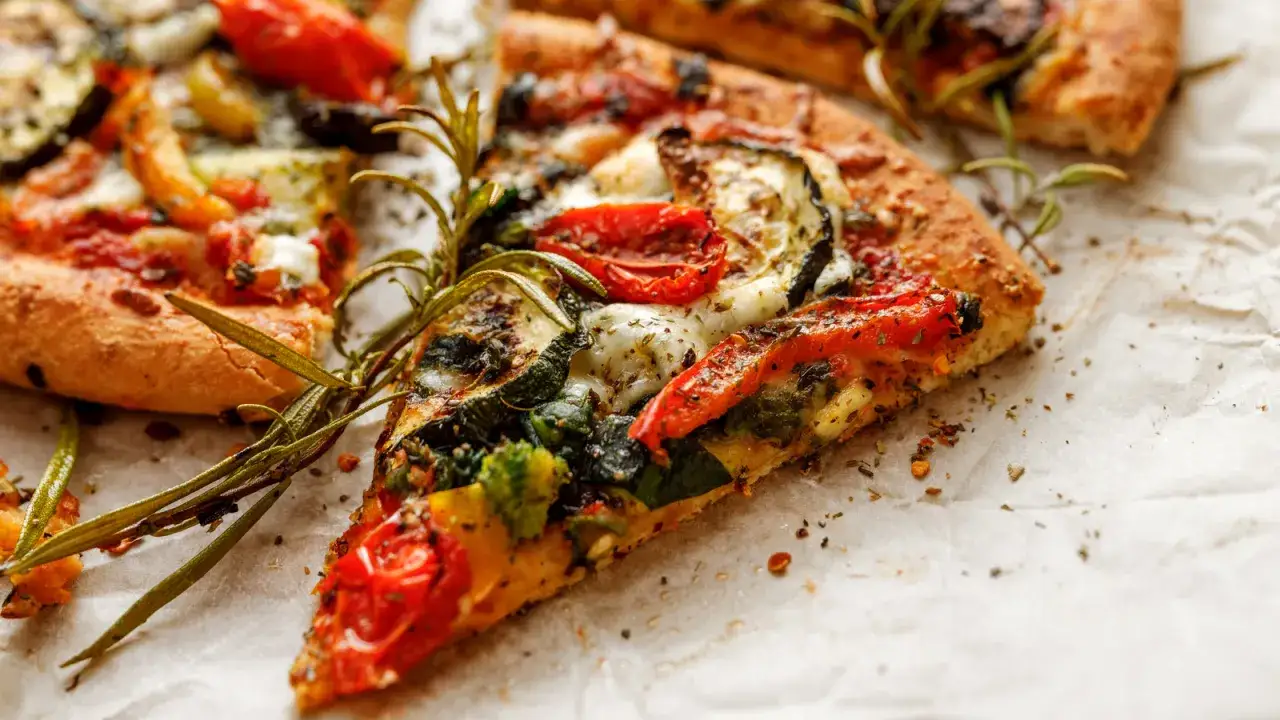 Kawałki pizzy gourmet z pomidorami, cukinią i rozmarynem na papierze.