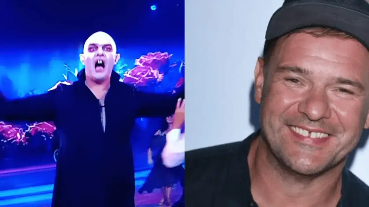 Tomasz Karolak w stroju wampira na scenie i uśmiechnięty w czapce.