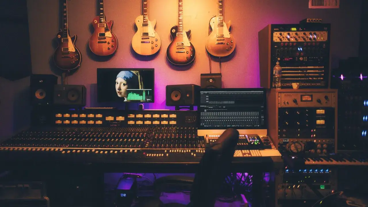 Estudio de grabación con guitarras colgadas, mesa de mezclas, monitores y un ordenador mostrando