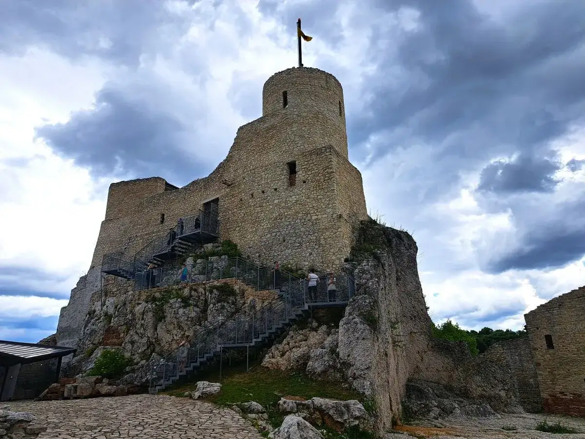 Kamienne ruiny zamku w Rabsztynie pną się na skalistym wzgórzu. Metalowe schody prowadzą turystów do historycznych zakamarków.