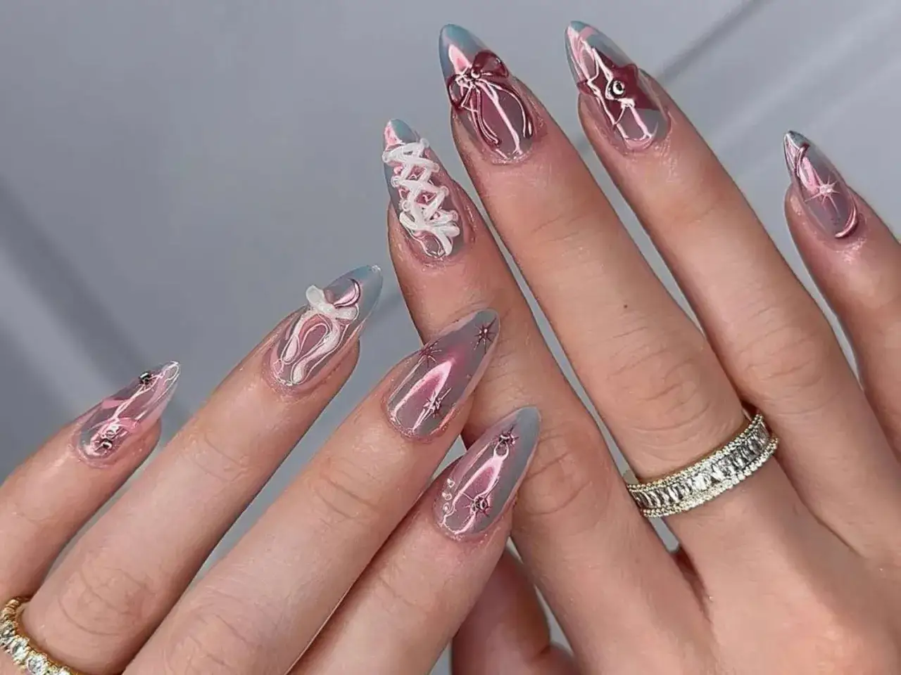 Unghie a mandorla con decorazioni tridimensionali a fiocco e stella, effetto metallizzato rosa e azzurro.