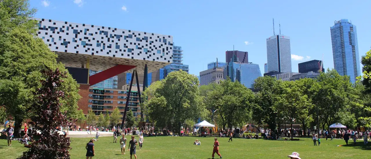 Un parc animé à Toronto, avec des étudiants de la Toronto Film School profitant du soleil près de bâtiments modernes.
