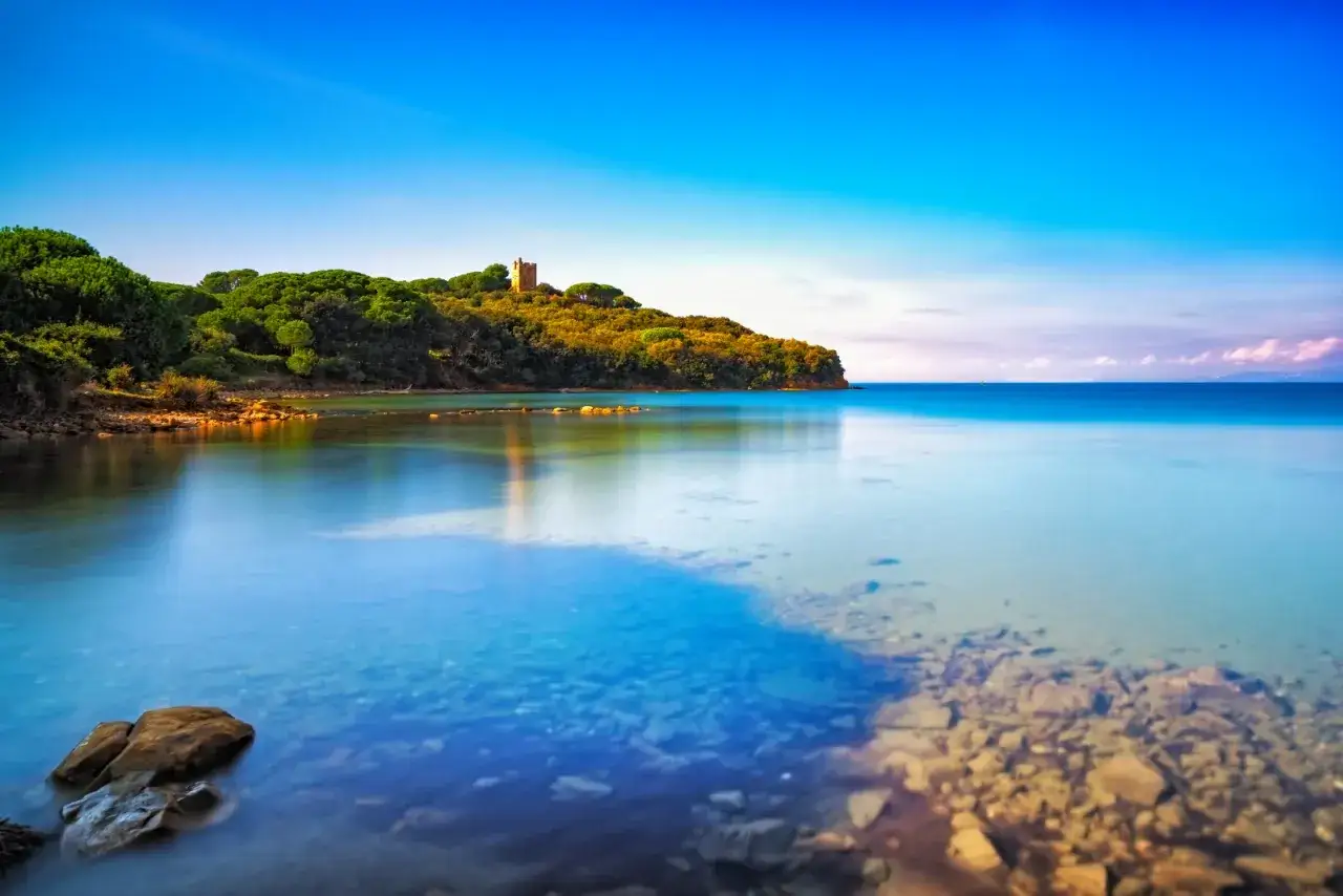 Torre medievale su una collina verdeggiante, con acque cristalline che lambiscono le **punta ala spiagge più belle**.