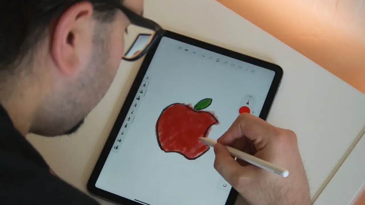 Mężczyzna tworzy rysowanie na iPadzie, używając Apple Pencil do namalowania czerwonego jabłka z zielonym listkiem.