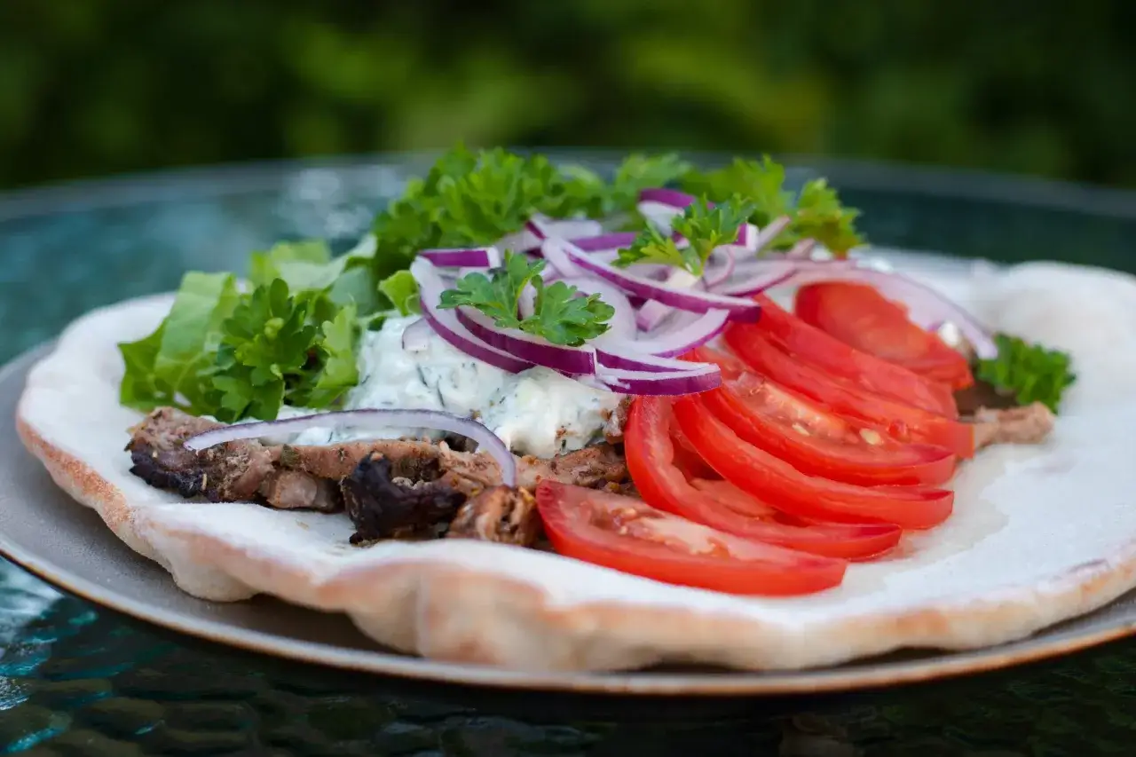En gyros med k&ouml;tt, tomater, r&ouml;dl&ouml;k, tzatziki och persilja p&aring; ett pitabr&ouml;d. Ett perfekt gyros recept f&ouml;r en sommardag.