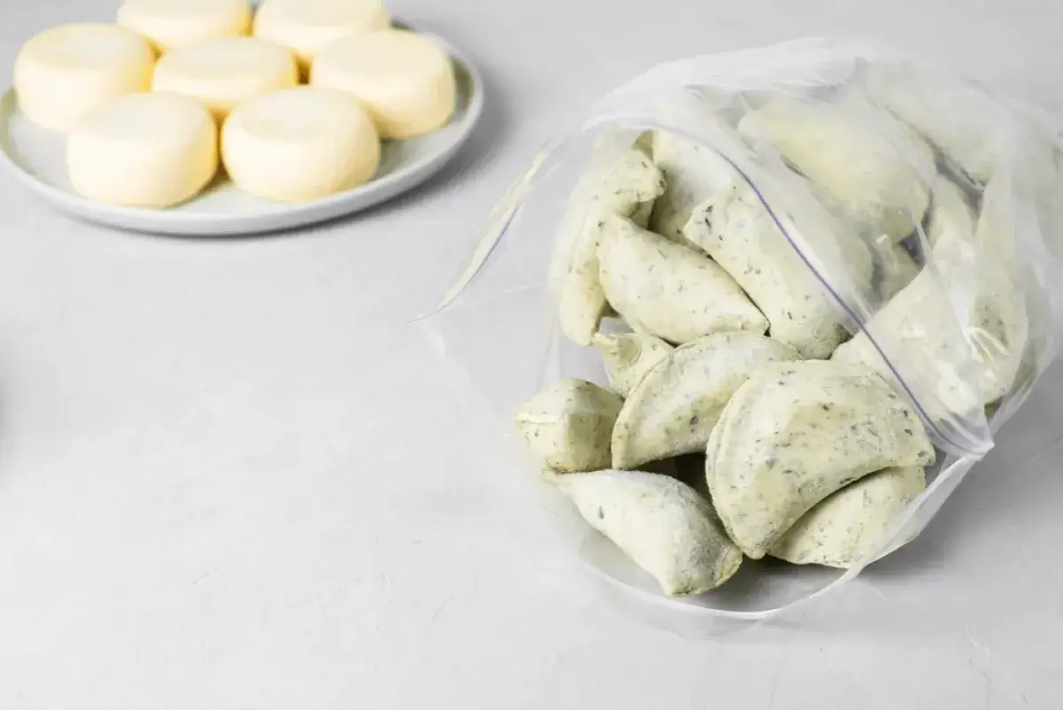 Gotowe do mrożenia pierogi w woreczku, obok talerz z okrągłymi serkami. Idealne, by dowiedzieć się, jak mrozić pierogi na później.