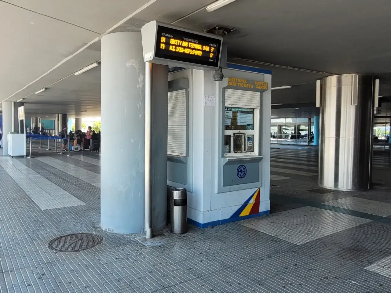 Tablica informacyjna na port lotniczy Saloniki Macedonia pokazuje odjazdy autobusów. Obok znajduje się budka z biletami.