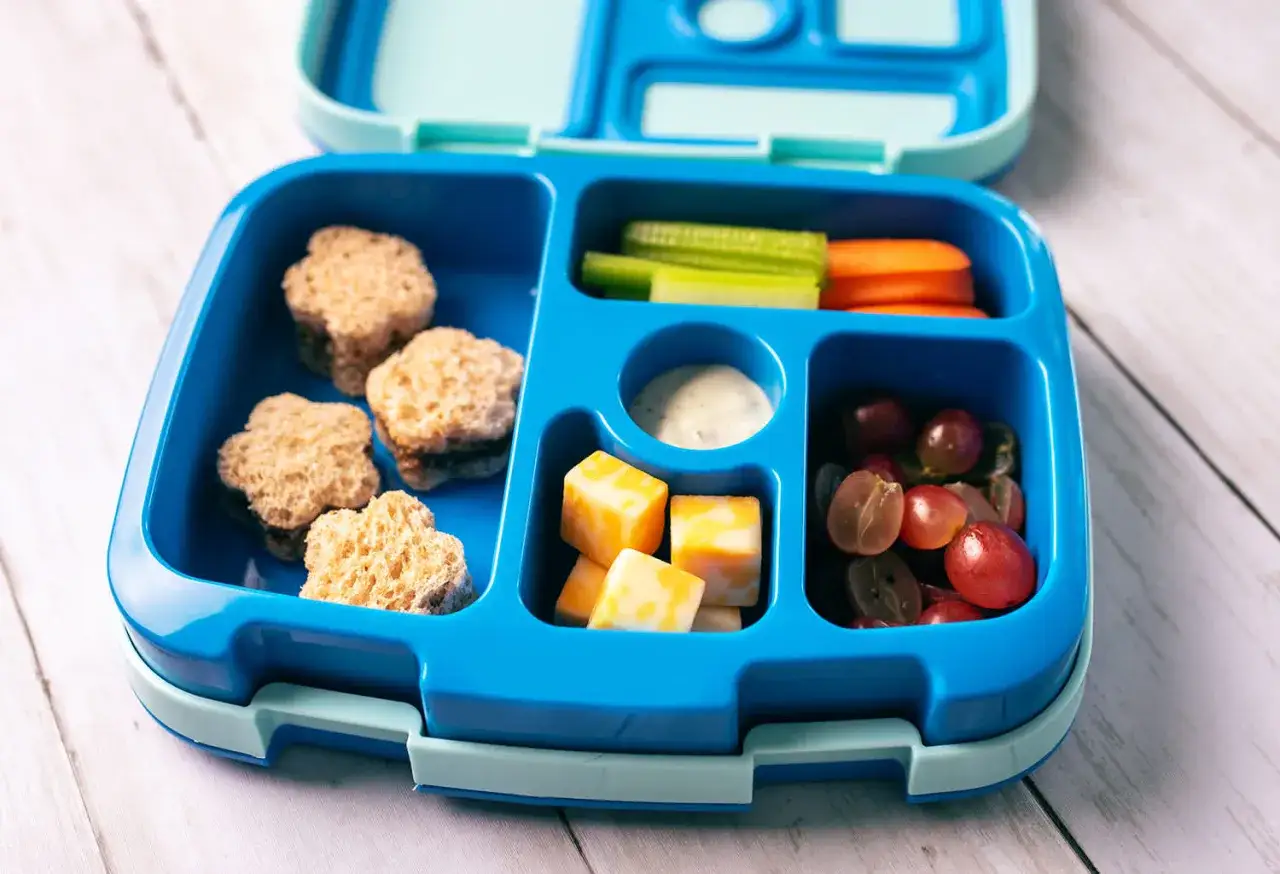 Kolorowy lunchbox z pysznymi, **zdrowymi przekąskami dla dzieci**: kanapki w kształcie gwiazdek, serek, winogrona, marchewka i seler.