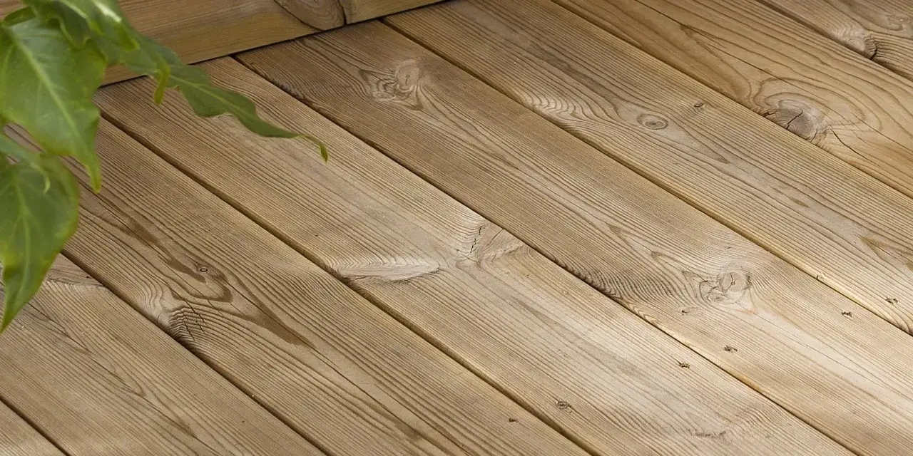 En närbild av en altan med trätrall. Gröna blad syns i övre vänstra hörnet. Perfekt för att betsa trall.