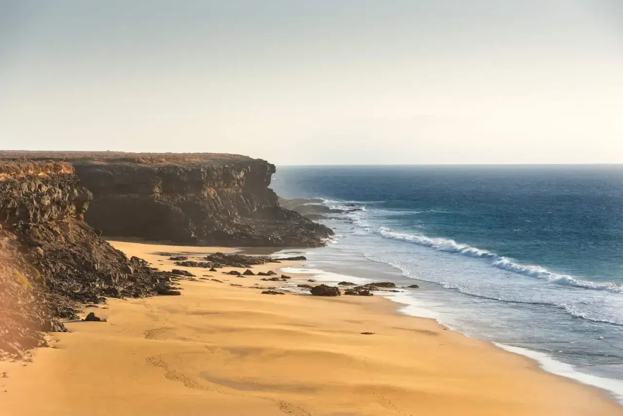 Goldener Sandstrand mit Felsen und Wellen. Das Wetter auf den Kanaren im Dezember ist oft sonnig und mild, ideal für einen Strandspaziergang.