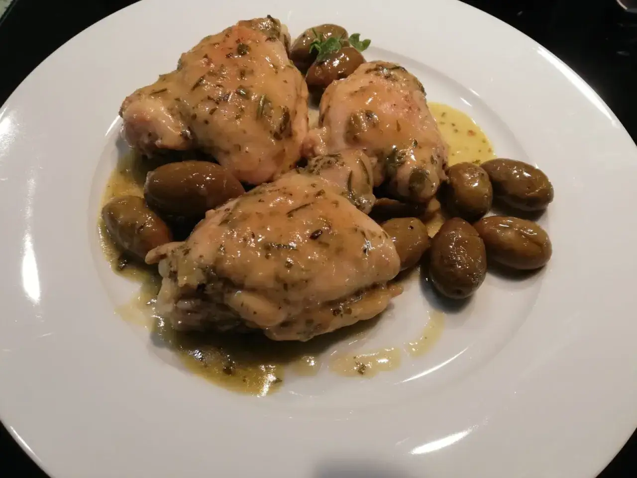 Tre succulenti pezzi di pollo al vino bianco, conditi con erbe aromatiche e serviti con olive verdi su un piatto bianco.