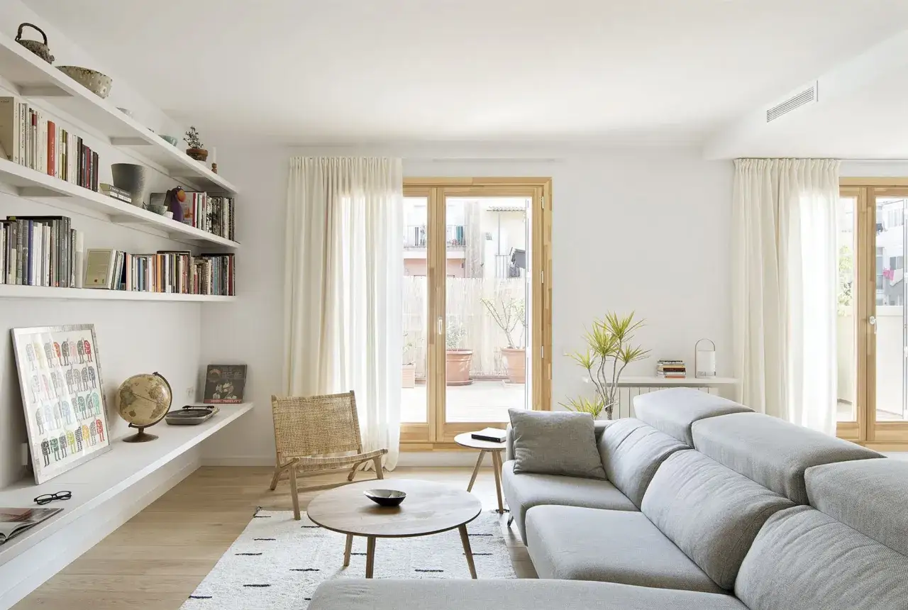 Un sal&oacute;n moderno con estanter&iacute;as llenas de libros, un sof&aacute; gris y una silla de mimbre. Unas sencillas salas peque&ntilde;as que invitan a la relajaci&oacute;n.