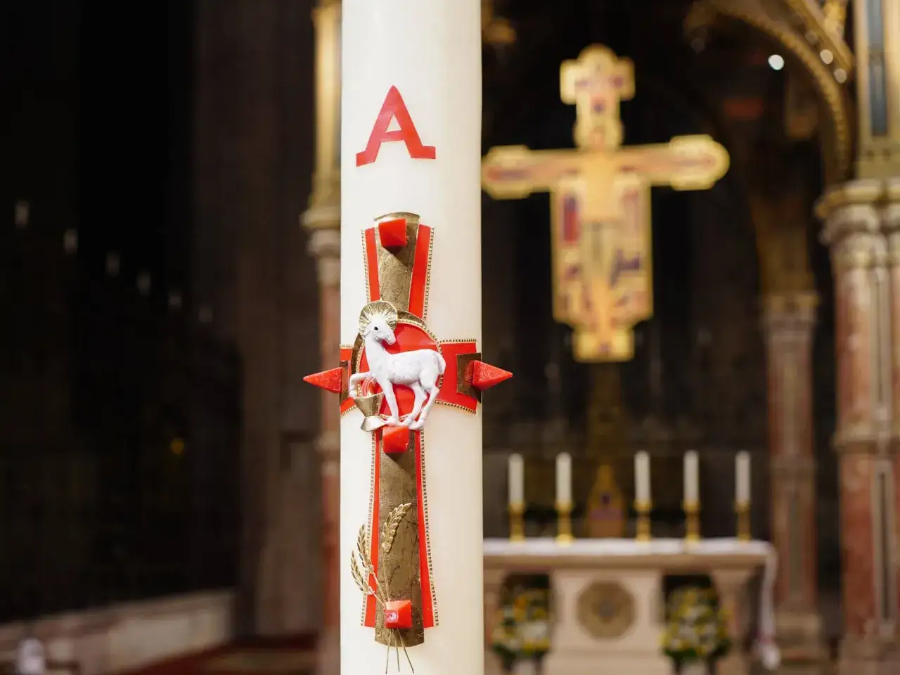 Osterkerze mit Lamm Gottes, ein wichtiges Symbol Ostern in der Kirche. Im Hintergrund ein Kreuz.