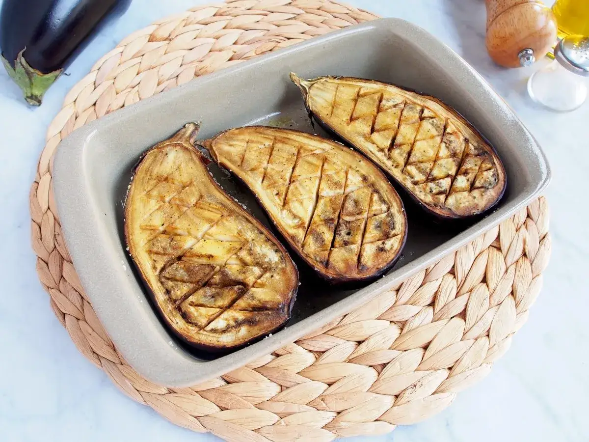 Berenjenas al horno, cortadas por la mitad y marcadas con un patrón de rejilla, listas para ser servidas.