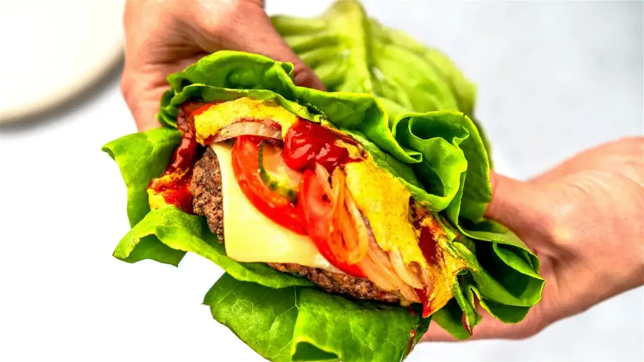 H&auml;nde halten eine Big Mac Rolle, eingewickelt in knackigen Salat. Saftiges Patty, K&auml;se, Tomaten, Zwiebeln, Ketchup und Senf.