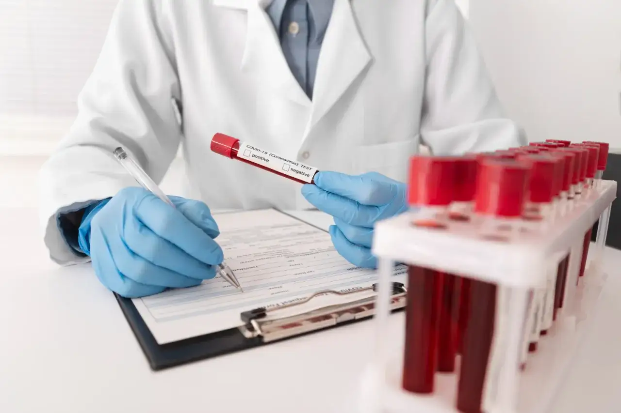 Laborant w rękawiczkach analizuje próbkę krwi do testu COVID-19, notując wyniki. Obok stoją probówki, czekając na analizę CRP norma.